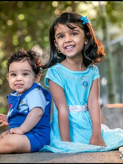 A brother and sister sitting together in a park. The natural lighting and their sweet expressions make this a beautiful and authentic outdoor sibling portrait.