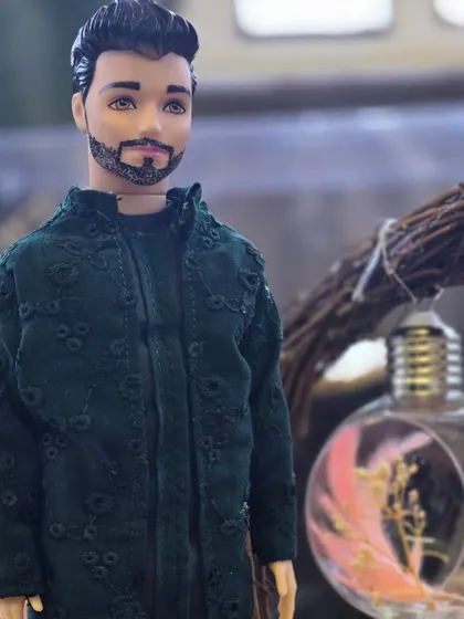 A close-up of a custom groom doll, showing the detailed embroidery on his dark green 'kurta'. We take pride in recreating every aspect of the original outfit.