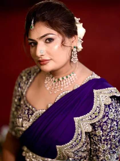 A portrait shot against a red background, which makes the purple saree and soft makeup pop.