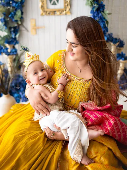 This mamma is glowing with happiness as she holds her little Krishna, dressed in a bright yellow outfit.