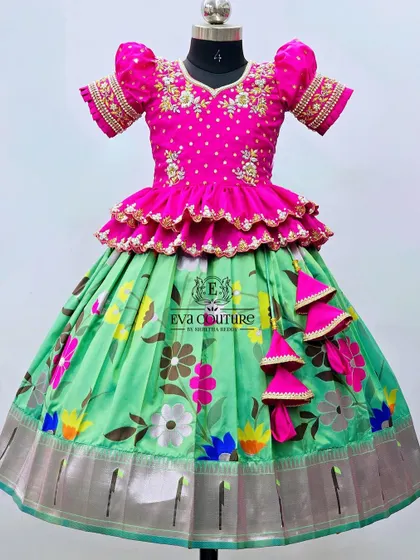 A beautiful floral lehenga with a pink peplum top. The blouse features heavy maggam work, and the green skirt has a colorful floral print and a silver zari border.