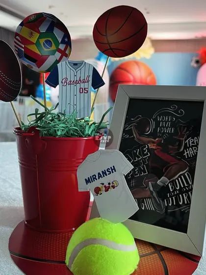 A close-up of a sports-themed centerpiece, including cutouts of a baseball jersey, a cricket ball, and a framed graphic of a basketball player.