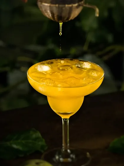 An action shot capturing a drop of passion fruit juice falling into the cocktail glass.