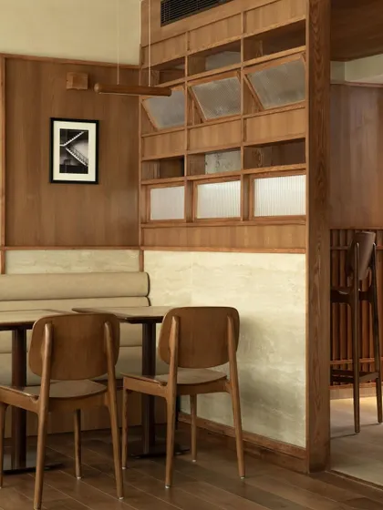 Seating nooks at QBF Coffee, where I used built-in banquettes and travertine wall panels to create comfortable, intimate zones. The large windows connect these serene interiors with the greenery outside.