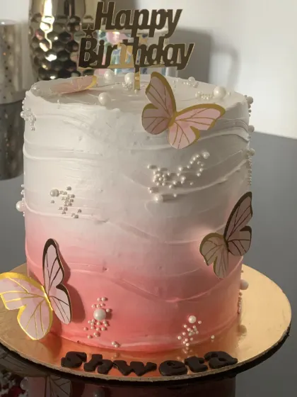 An elegant ombre cake for a birthday. The pink and white gradient is complemented by delicate butterflies and a gold "Happy Birthday" topper.