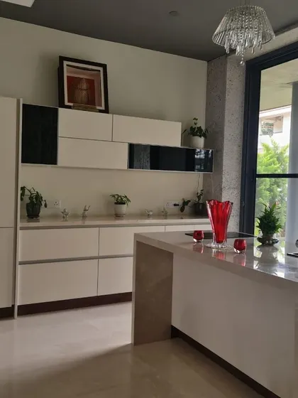 This minimalist kitchen features handleless white cabinetry, a sleek island, and a large window that brings in natural light. A pop of red from a vase adds a touch of vibrant color to the serene space.