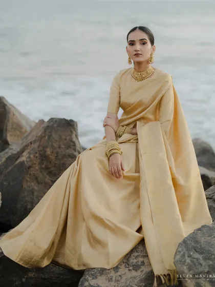 Seated by the sea, a portrait of calm and elegance. The bride's golden saree complements the natural, rugged beauty of the rocks and the soft light of the ocean.