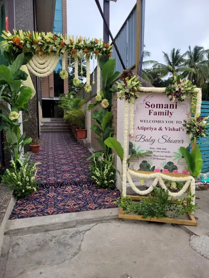 A beautiful entrance arrangement for a baby shower, featuring a floral arch with hanging jasmine strings and a personalized welcome sign for the family. The pathway is lined with greenery to guide guests into the venue.