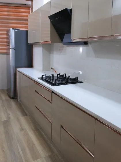 A look at a completed modular kitchen project, featuring glossy beige cabinets, a sleek black chimney, and handle-less drawers for a clean, modern aesthetic.