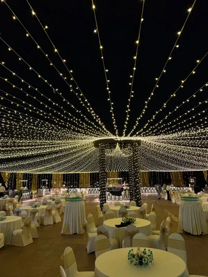 An outdoor dining area transformed by a vast ceiling of fairy lights, creating a magical and romantic ambiance for an evening reception.