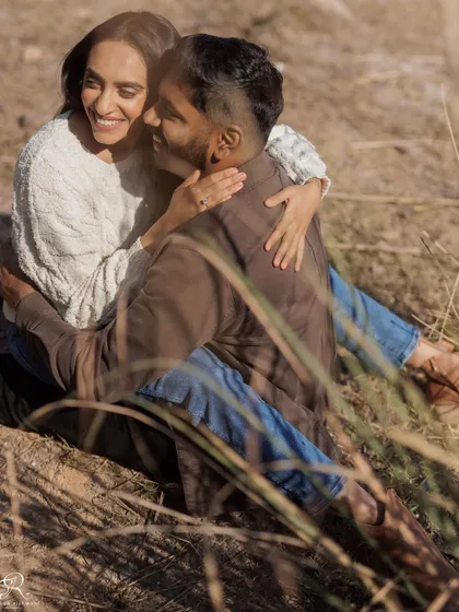 A lovely, relaxed moment of the couple sitting together in a field of dry grass. The warm sunlight and their comfortable embrace create a cozy and romantic atmosphere.