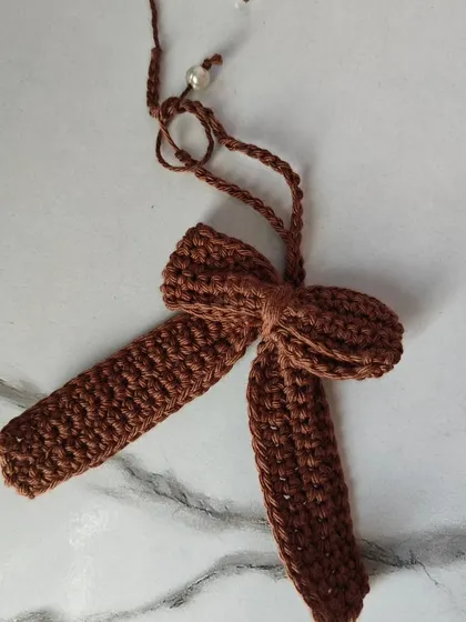 A close-up of the earthy brown crochet bow. The craftsmanship ensures it is a durable and beautiful accessory that will last.