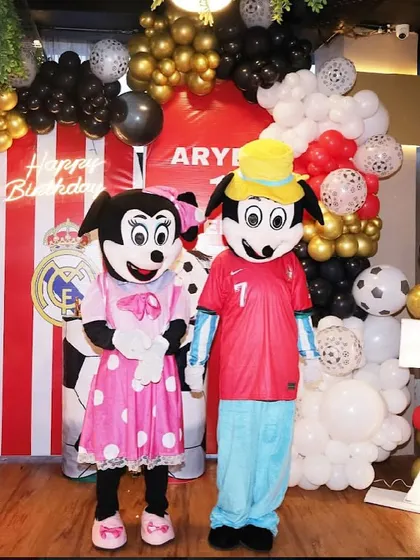 Mickey and Minnie mascots pose in front of a football-themed backdrop, ready to celebrate with the birthday boy.