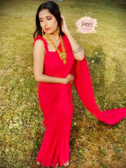 A stunning celebrity photoshoot featuring a model in a flowing red saree. The makeup is bold and dramatic to create a high-fashion look.