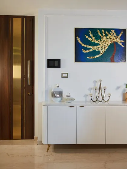 This minimal console with a marble top and PU shutters blends seamlessly with dining setups. It is styled with a piece of art and a modern candelabra.