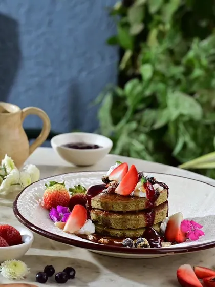 A stack of my healthy millet pancakes, adorned with fresh fruit and flowers.