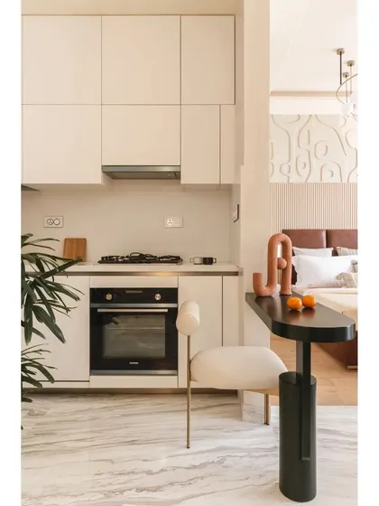 The compact kitchen and dining nook are seamlessly integrated into the open-plan layout. A sleek black table serves as a dining spot, connecting the kitchen to the bedroom area in a fluid, functional way.