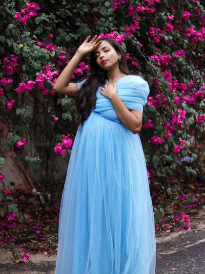A lovely pose in the light blue tulle maternity gown. The soft fabric and color complement the natural floral background, ideal for an outdoor pregnancy photoshoot.