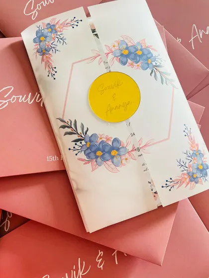This modern invitation features a vellum wrap with a watercolor floral design, held together by a bright yellow acrylic seal.