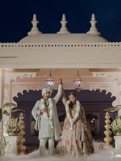 A triumphant moment for the newlyweds against the stunning architecture of their Udaipur wedding venue. The smoke effect and grand setting create a truly cinematic celebration shot.