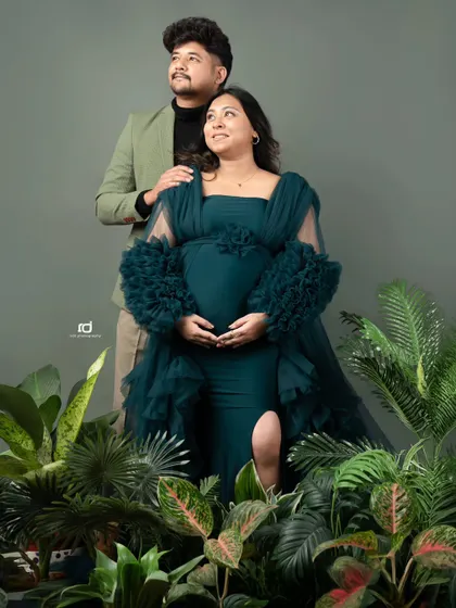 A stylish and modern maternity portrait. The deep green gown and botanical props give this studio shot a sophisticated and natural feel.