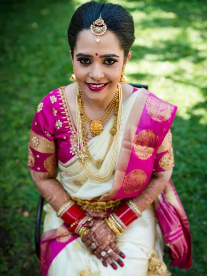 A beautiful portrait of a South Indian bride in her traditional white and pink silk saree, smiling brightly.