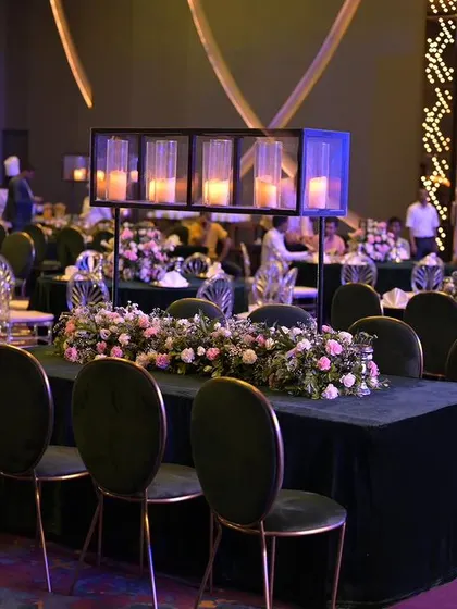 A closer look at the table settings for the gala dinner, featuring dark tablecloths, elegant floral runners, and modern candle holders. The contrast between the dark tables and soft florals adds a contemporary and stylish touch.