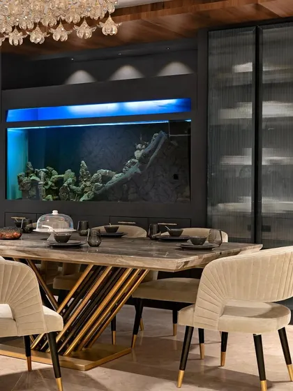 The dining space is anchored by a large aquarium integrated into the crockery unit, adding a dynamic and calming element. The design combines bespoke furniture, elegant lighting, and functional storage to create a sophisticated dining experience.
