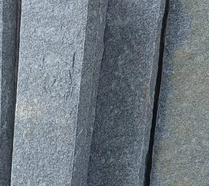 Stacks of dark grey natural stone pillars, ready for use in construction or landscaping.