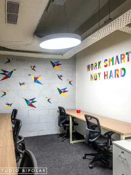 This dedicated workstation area features colorful origami bird decals and a 'Work Smart Not Hard' graphic on the wall. These playful details on a concrete-finish wall create a modern and inspiring environment for focused tasks.