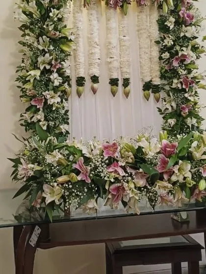 A close-up of the Ganpati decoration made with pink and white lilies, with hanging tuberose (rajnigandha) garlands against a white curtain.