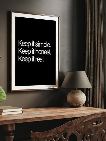 The "Keep it simple" print in a classic frame, placed on a dark wood desk. It serves as a perfect, grounding reminder in a home office or study.