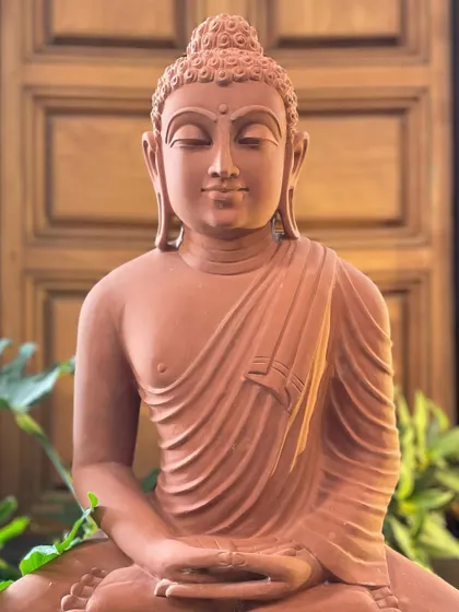 A close-up of our red sandstone meditating Buddha, highlighting the calm expression and the texture of the handcrafted stone.