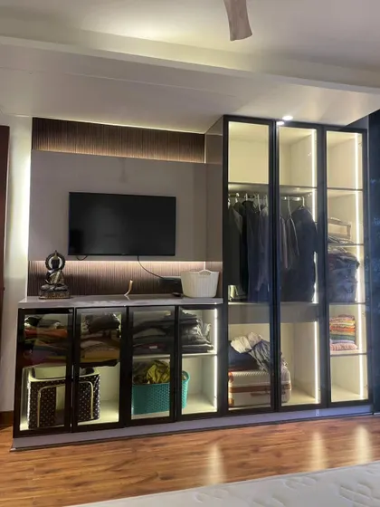 A multi-functional bedroom unit that combines a TV console, open shelves, and a wardrobe with glass doors. The integrated lighting highlights the display items and adds a warm ambiance.