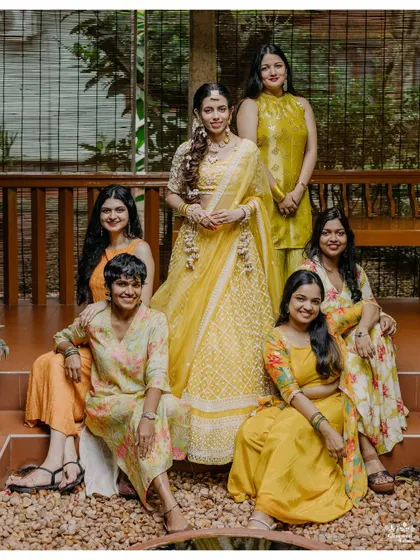The bride and her bridesmaids, all dressed in coordinated yellow and orange outfits, share a happy moment together.
