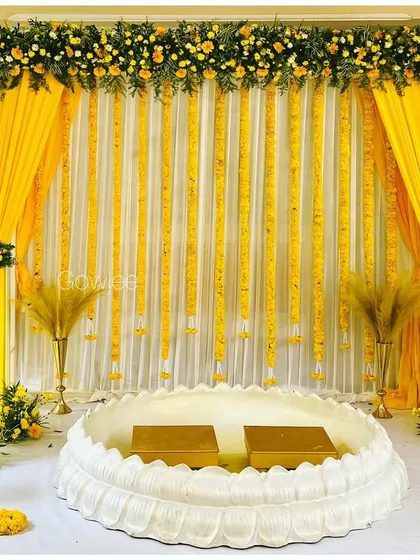 A classic and elegant Haldi stage setup with a lotus-shaped seating and beautiful marigold decor.