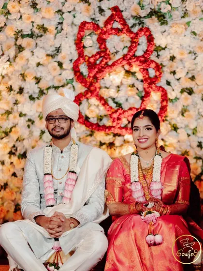 The couple seated before a beautiful floral Ganesha backdrop at their wedding ceremony.