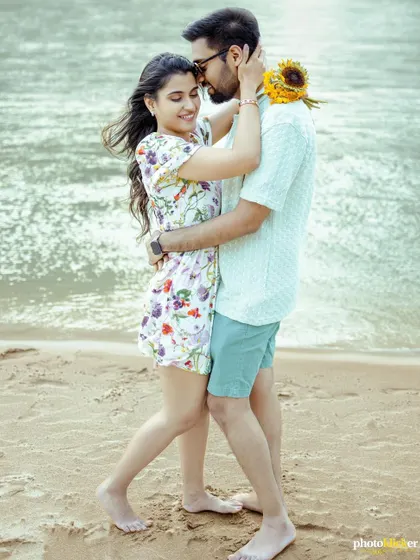 A sweet and romantic embrace on the beach, with the woman wrapping her arms around her partner, holding a sunflower.