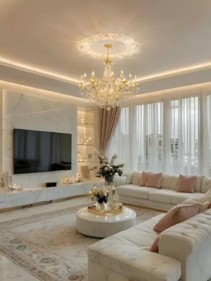 A truly luxurious living room featuring a tufted white sectional, a marble-clad TV wall with integrated shelving, and a classic crystal chandelier. The design exudes opulence and grandeur, perfect for making a statement.