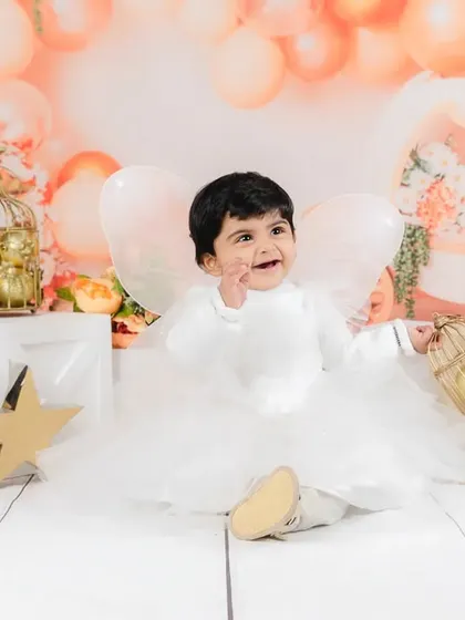 A happy baby boy, dressed as an angel, plays with a prop during his first birthday photoshoot. His smile is pure magic.