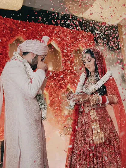 A shower of petals rains down on the couple during their jaimala, a moment of pure celebration and joy against a stunning backdrop of red flowers.