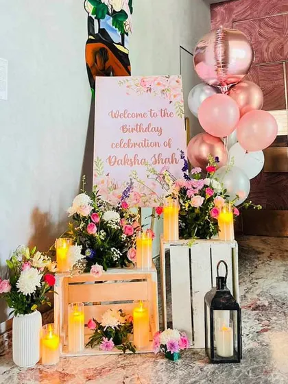 A charming welcome corner for a birthday celebration. We combined a floral welcome sign with fresh flower arrangements on wooden crates, candles, and a bunch of helium balloons.