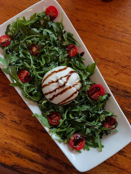 A top-down view of our Burrata salad, with fresh arugula, cherry tomatoes, and a balsamic glaze.
