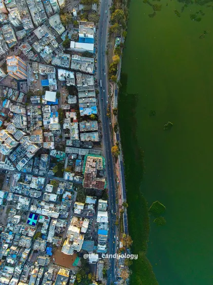 The city of Dahod meets the green waters of a lake. This shot highlights the sharp contrast between the urban environment and the natural landscape it borders.