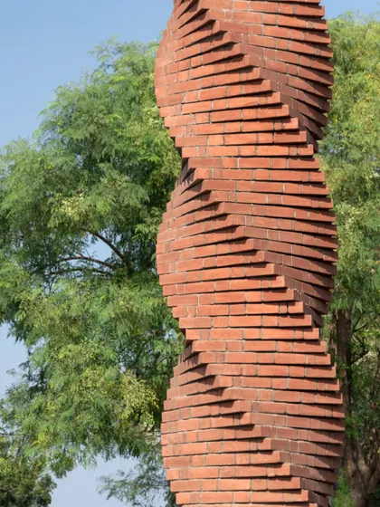 **The Urban Twist, Ahmedabad:** The texture of the brick is prominent in this shot, contrasting with the soft foliage of the trees. The column is designed to be a quiet, grounding pause in the busy urban landscape.