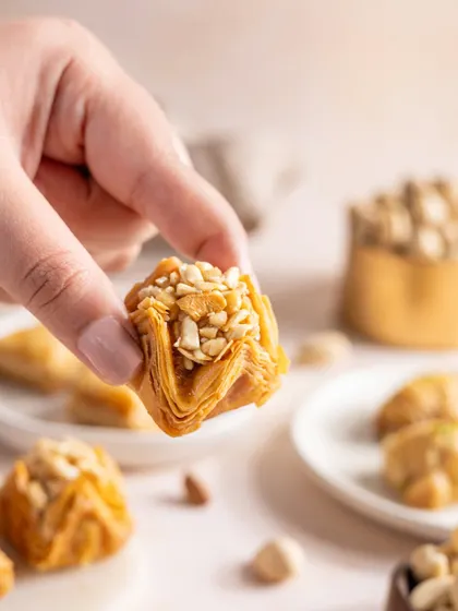 A hand holding a piece of baklava, making the dessert feel accessible and tempting.