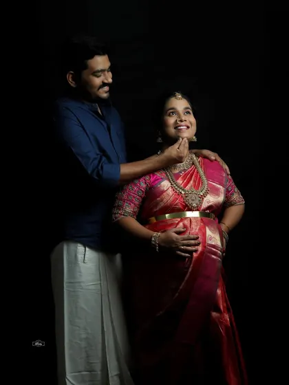 A joyful interaction between a couple during their traditional maternity session. The dark studio background makes their expressions and beautiful attire stand out.