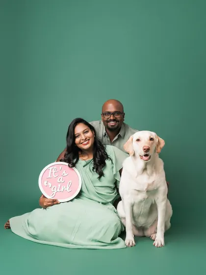 The whole family joins in for the big reveal. This portrait captures the joy of the expecting parents and their very happy dog against a clean studio backdrop.