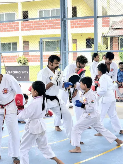 A student practices their sparring technique with an instructor holding pads during the karate exam.