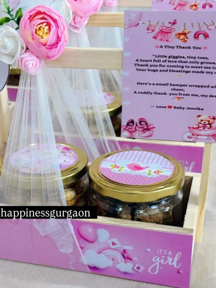 This image focuses on a single pink announcement basket, highlighting the custom "It's a girl" design and the floral embellishments.